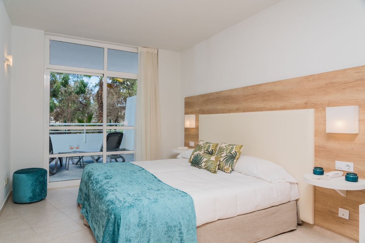Bedroom with blue bedspread, tropical pillows, and balcony view in Tenerife.