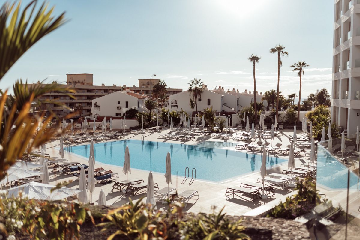 Outdoor pool surrounded by sun loungers and palm trees in Tenerife.
