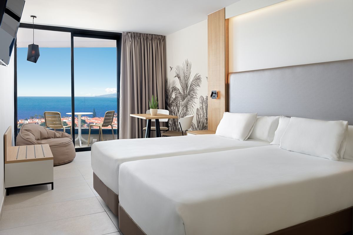 Hotel room with twin beds, table, chairs, and view of ocean in Tenerife.