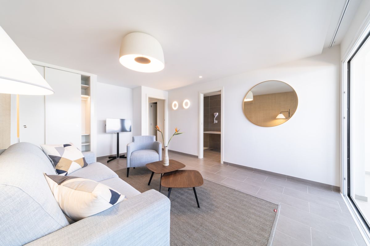 Modern living room with gray sofa, armchair, TV, and round mirror in Tenerife apartment.