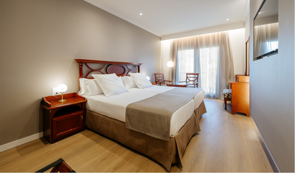 Two beds with wooden headboards in a hotel room in Tenerife, with chairs and a TV.