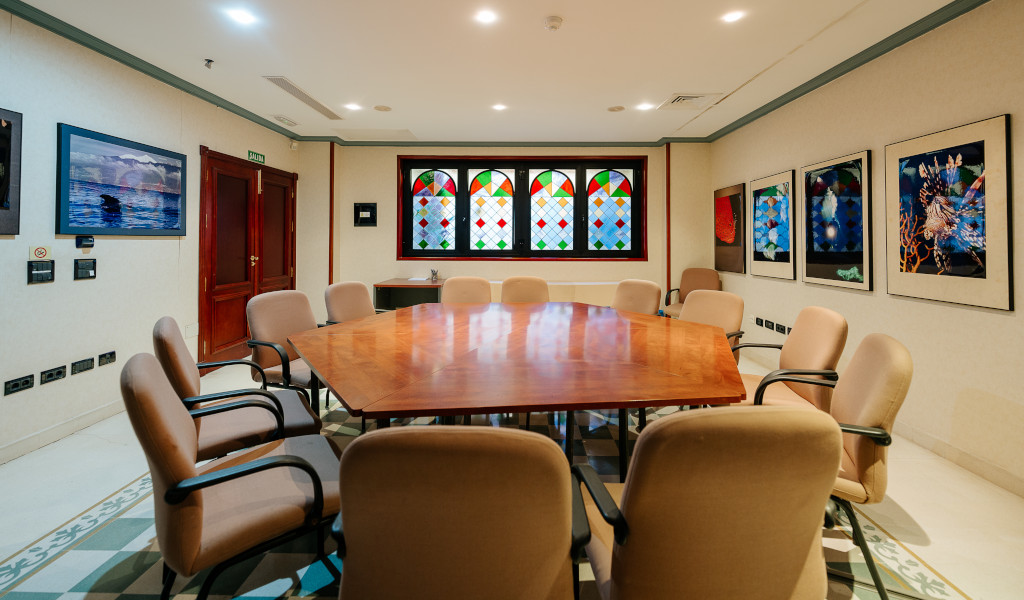 Meeting room with a wooden table, beige chairs, stained glass window, and framed art in Tenerife.