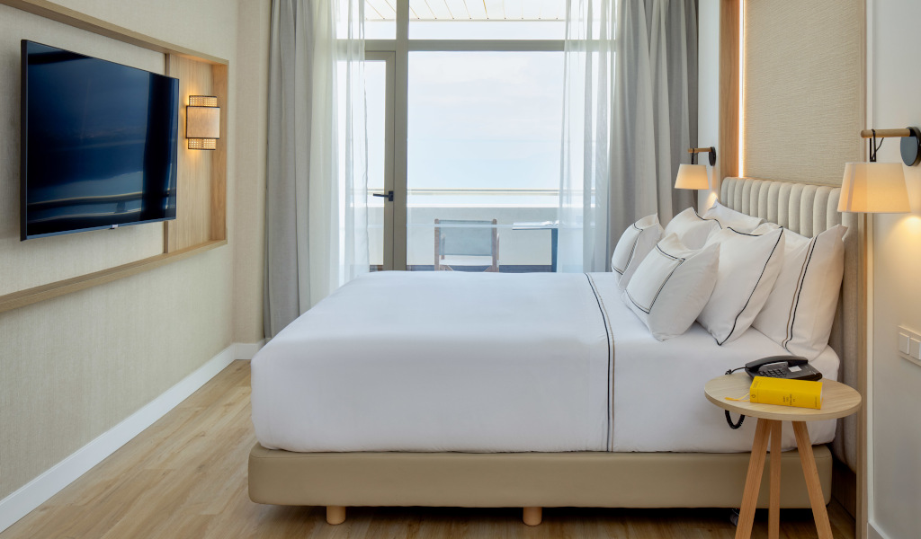 Hotel room in Tenerife with bed, side table and wall-mounted TV, ocean view.