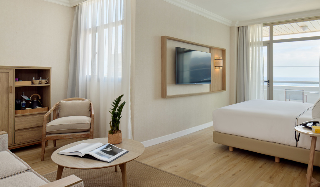 Hotel room with bed, TV, chair, and ocean view in Tenerife.