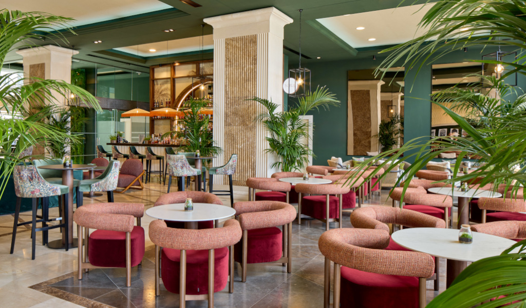 Cafe lounge with tables, chairs, and plants in Tenerife hotel.