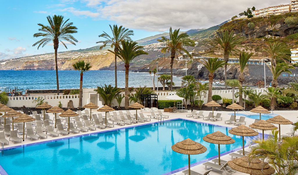 Swimming pool with sunbeds and umbrellas overlooking the ocean in Tenerife.