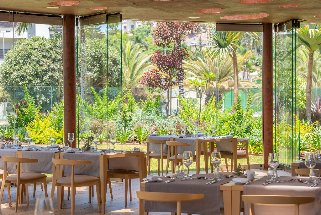 Restaurant with glass walls overlooking gardens in Tenerife. Tables set with glassware.