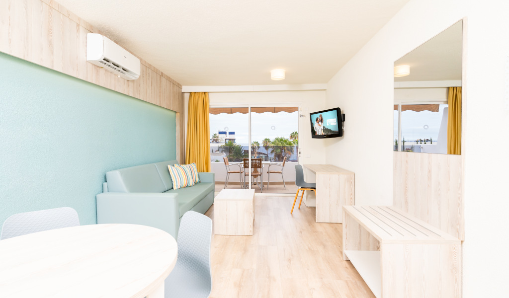 Bright living room with sofa, table, and wall-mounted TV, overlooking a balcony in Tenerife.
