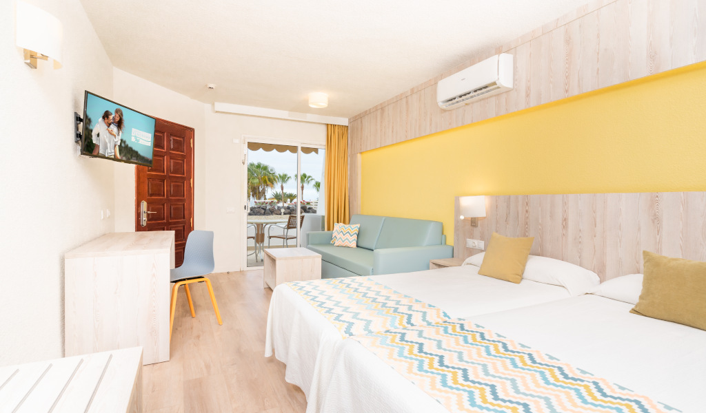 Hotel room with two beds, sofa, TV, and terrace view at La Laguna, Tenerife.