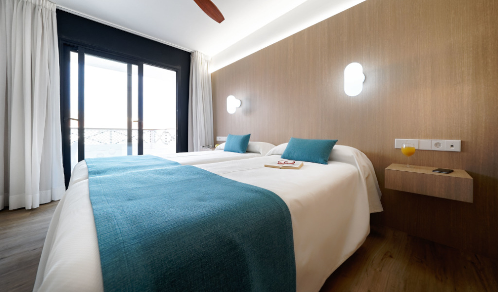 Hotel room with twin beds, wooden wall, and a balcony view in Tenerife.
