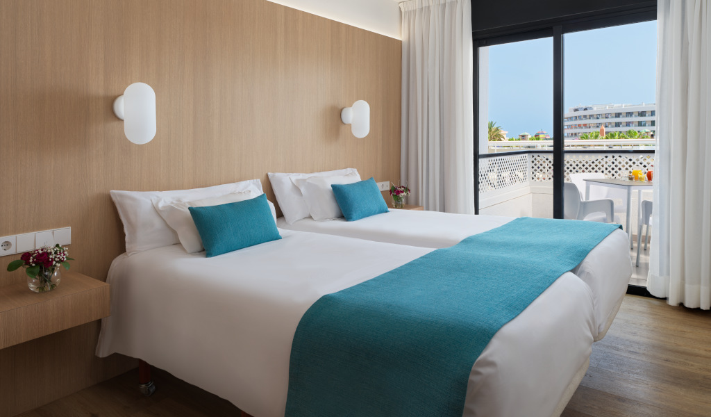 Two beds with blue blankets in a hotel room in Tenerife, view of a terrace.
