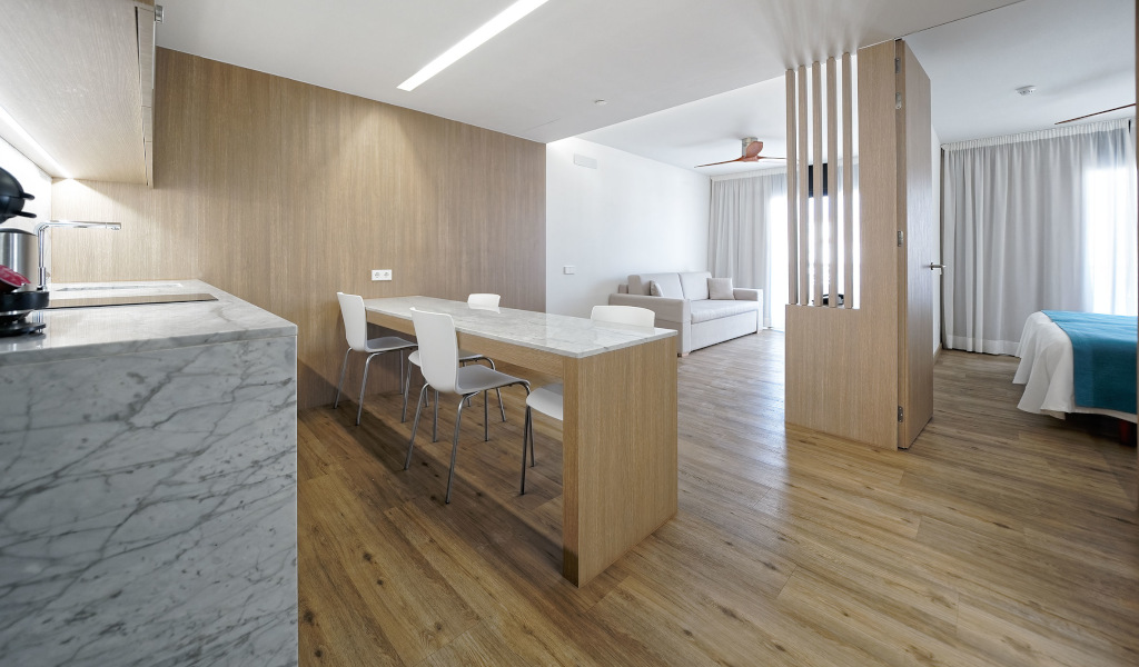 Open-plan hotel room in Tenerife with kitchen, dining table, and sofa area.