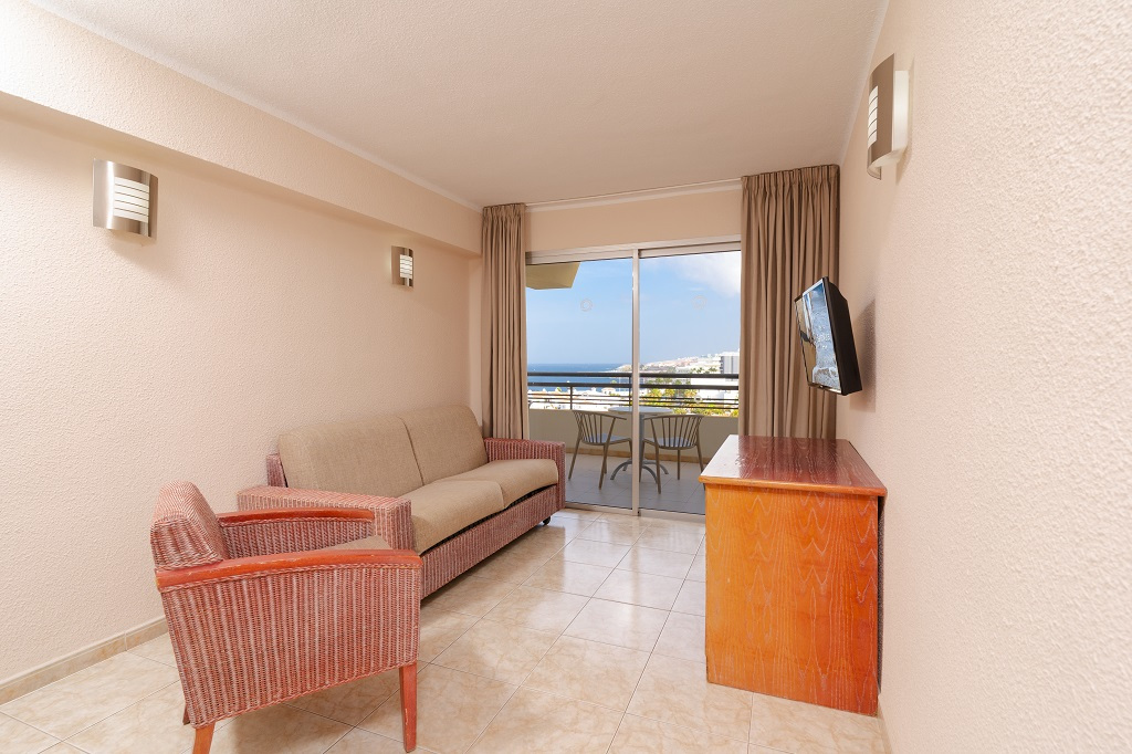 Living room with sofa, armchair, TV, and balcony view in Tenerife apartment.