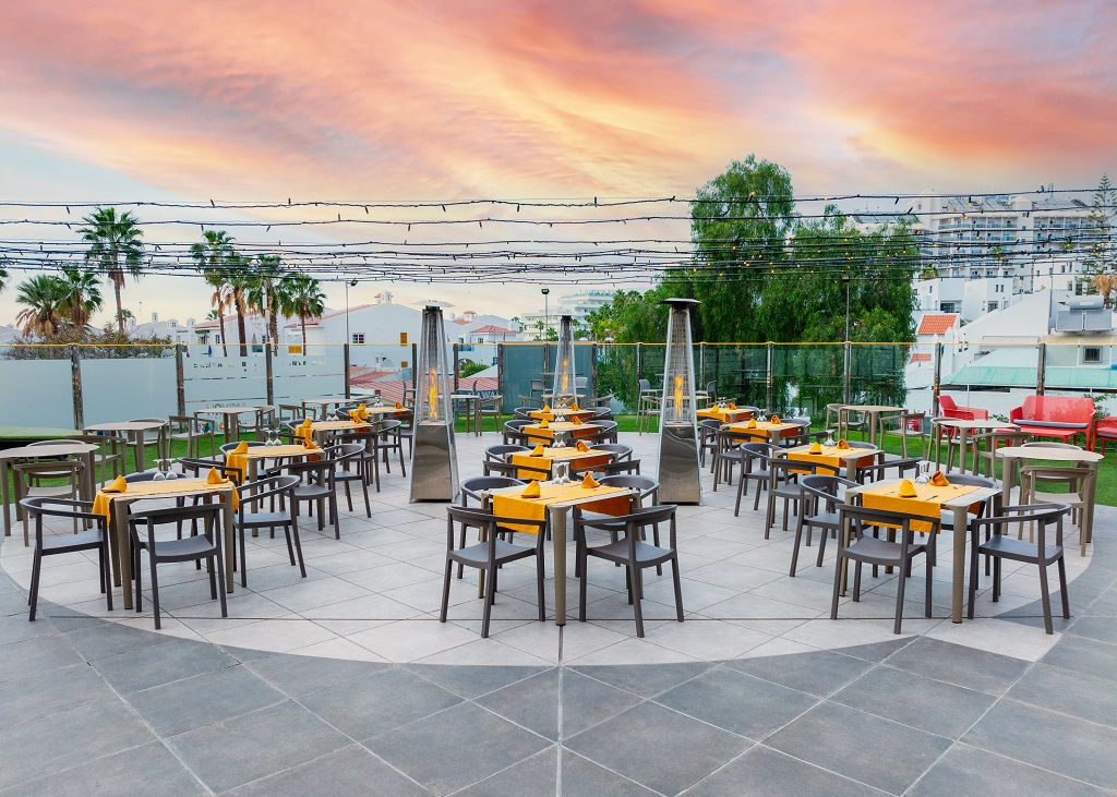 Outdoor dining area with arranged tables and chairs in Tenerife at sunset.