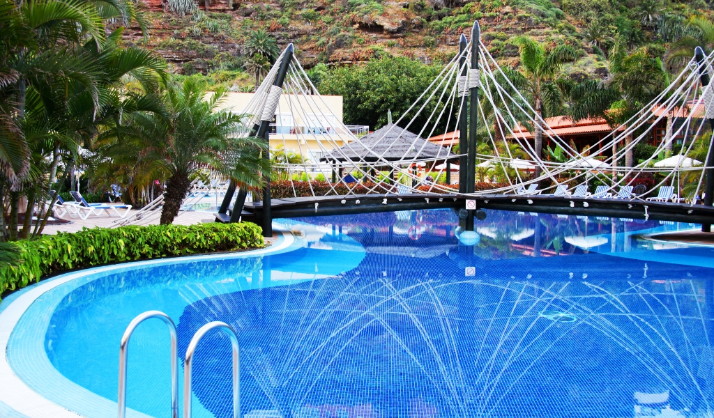 Outdoor pool with rope bridge and tropical plants at a Tenerife resort.