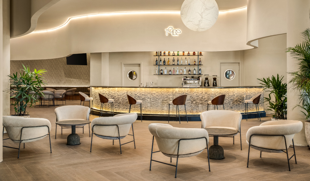 Modern bar interior with cushioned chairs, a lit bar counter, and bottles displayed on shelves.