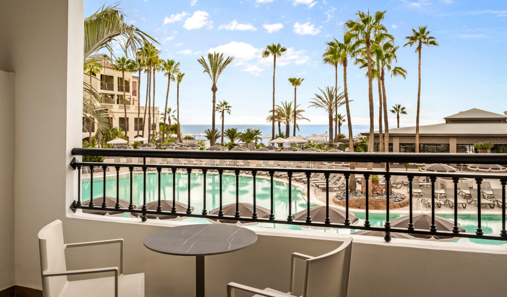 Balcony view of a swimming pool and palm trees at a Tenerife resort.