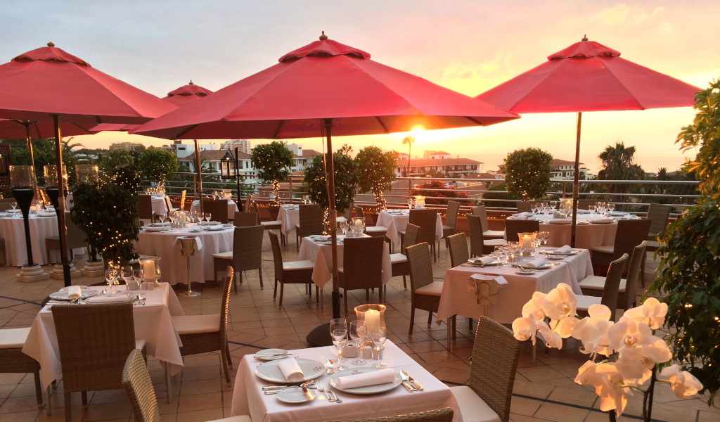 Outdoor dining area with red umbrellas at sunset in Tenerife.