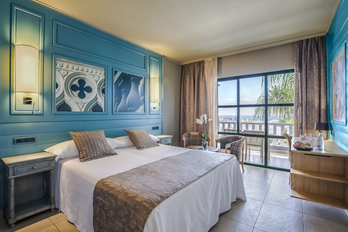 Hotel room with double bed, balcony view of Santa Cruz de Tenerife, and two armchairs.