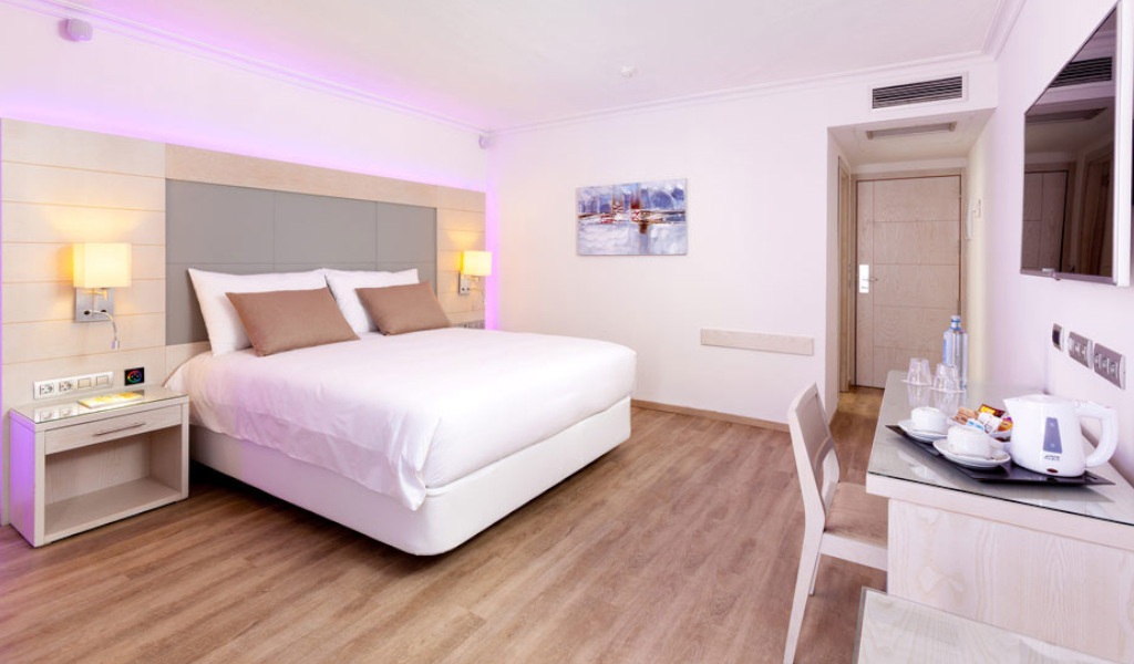 Modern hotel room with double bed, nightstands, a painting, and a desk in Tenerife.