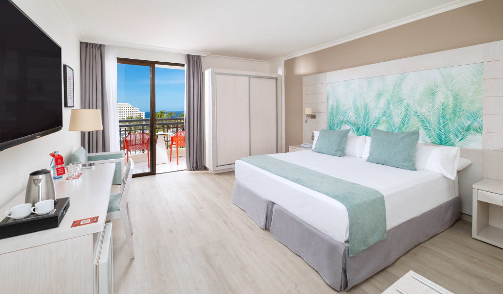 Hotel room with double bed, balcony view of Costa Adeje, and light decor.