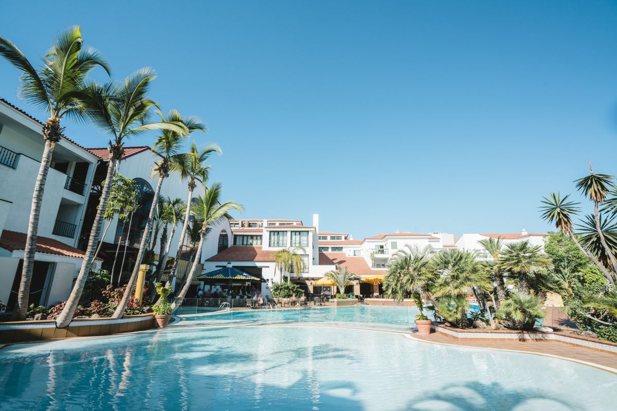 Outdoor pool with palm trees and buildings in Tenerife resort.