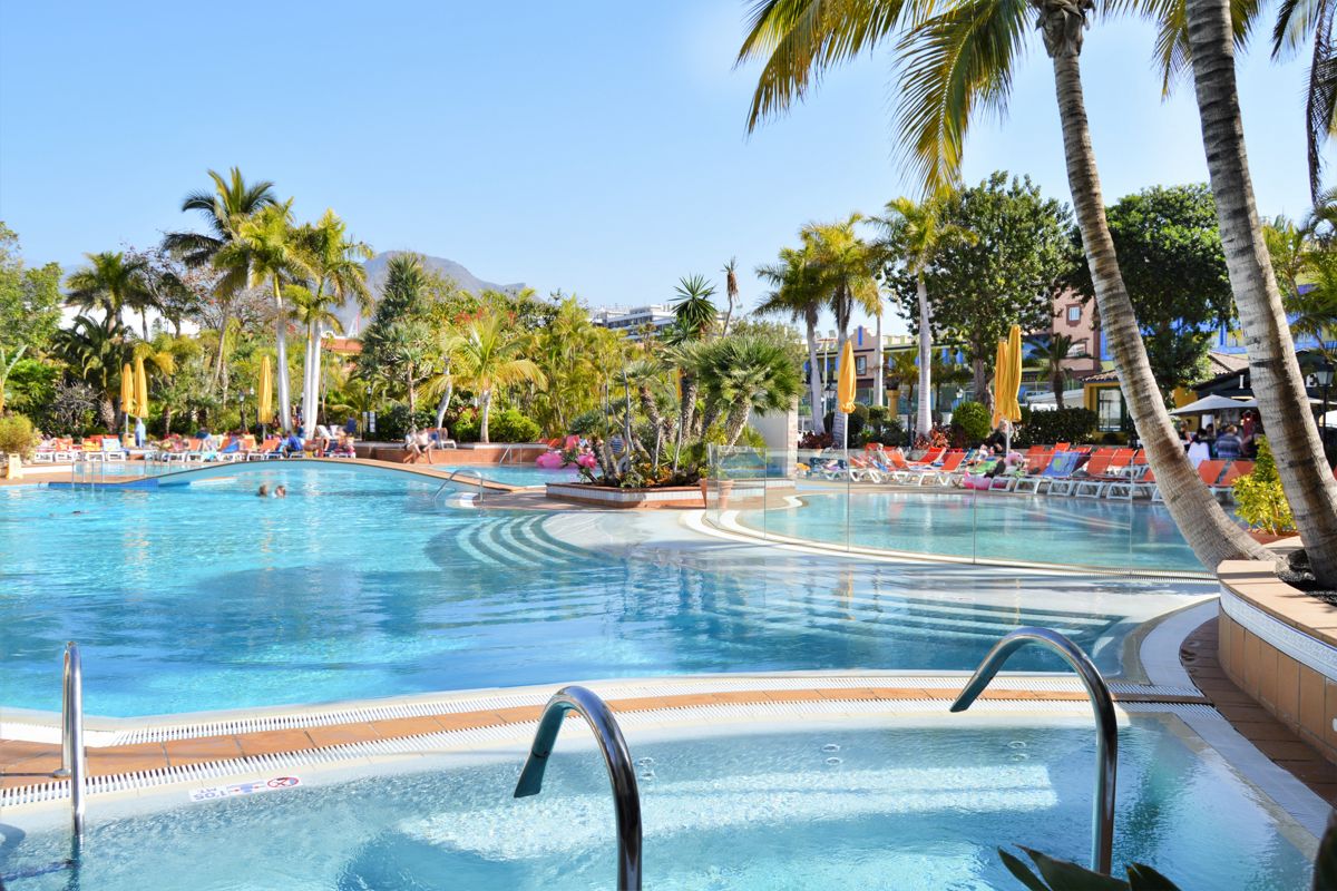 Outdoor pool area with sun loungers and palm trees in Tenerife resort.