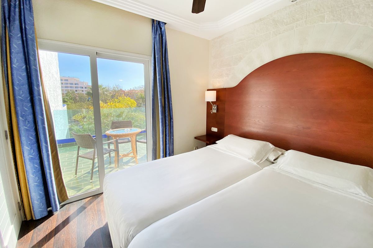 Two beds in a hotel room with balcony view in Tenerife.