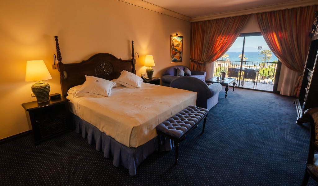 Hotel room in Tenerife with double bed, sofa, and balcony view of the sea.