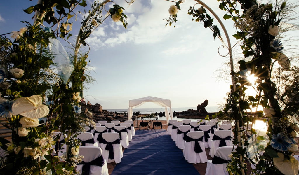 Wedding ceremony setup by the sea in Tenerife with white and black decorated chairs.