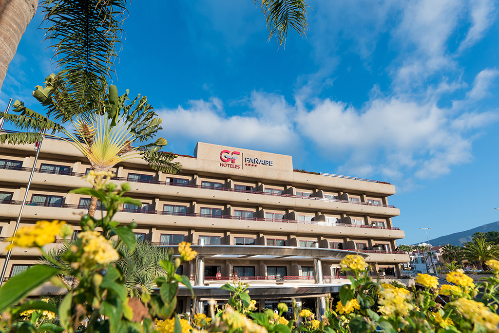 GF Fañabé hotel building in Tenerife with flowers and palm tree in foreground.