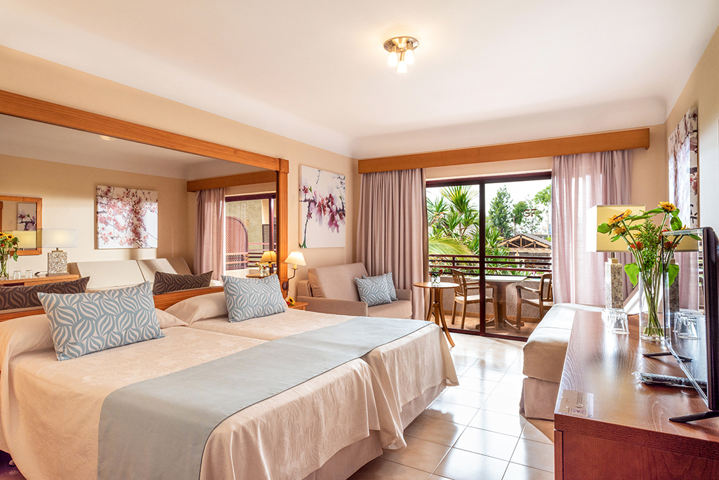 Hotel room with two beds, sofa, table, and balcony view in Tenerife.