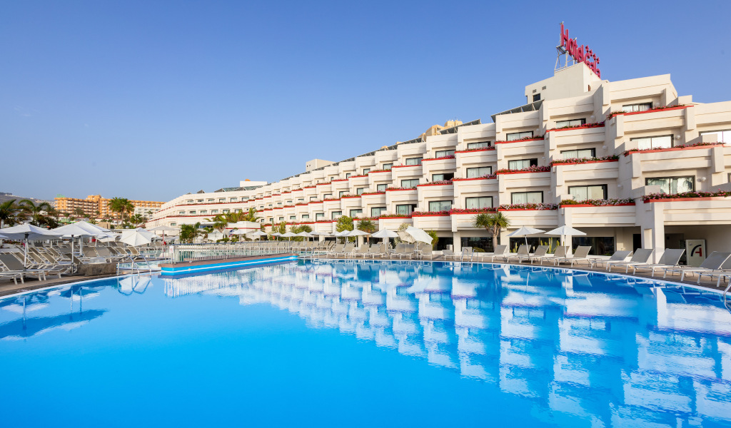 Outdoor pool with sun loungers at a hotel in Tenerife, reflecting modern white building.