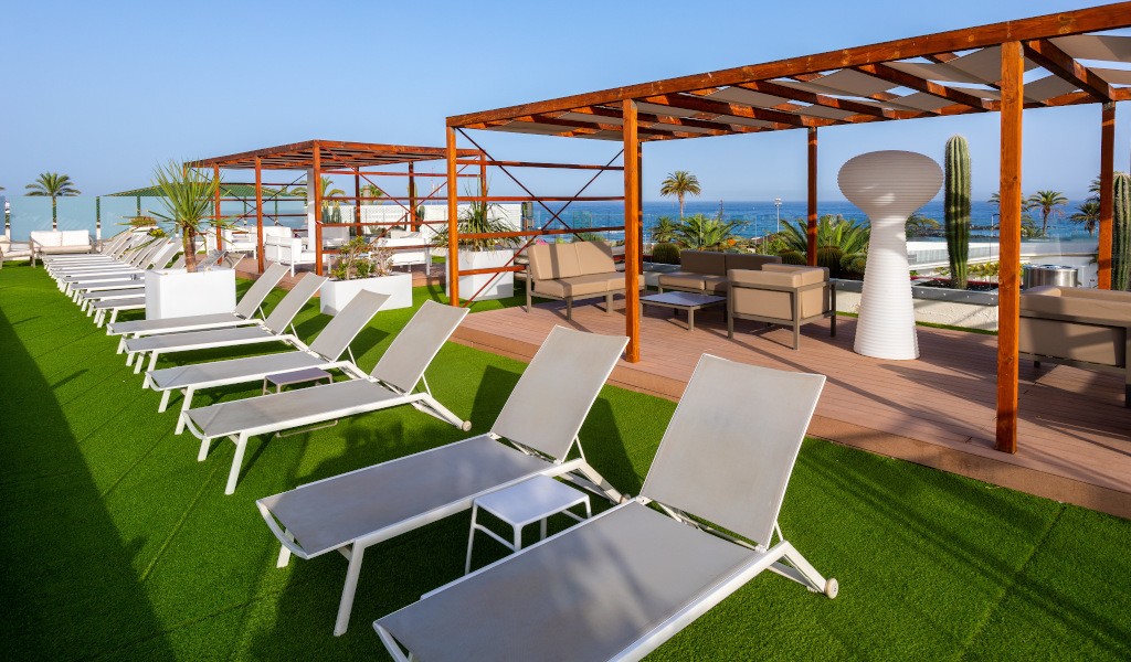 Sun loungers on a rooftop terrace in Tenerife with ocean view and palm trees.