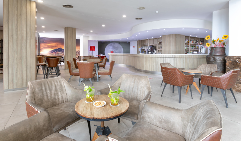 Modern seating area with wooden tables, drinks, and snacks in a Tenerife hotel lounge.