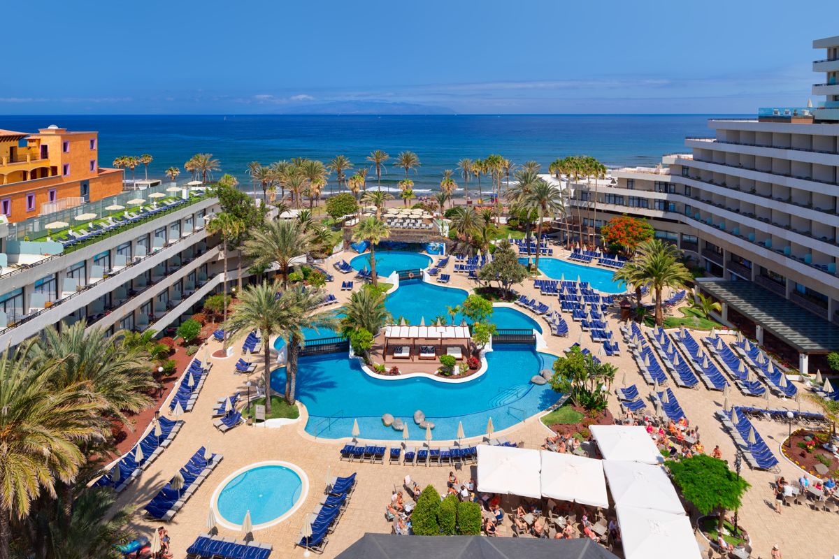 Swimming pool and lounge chairs at a Tenerife hotel with ocean view.