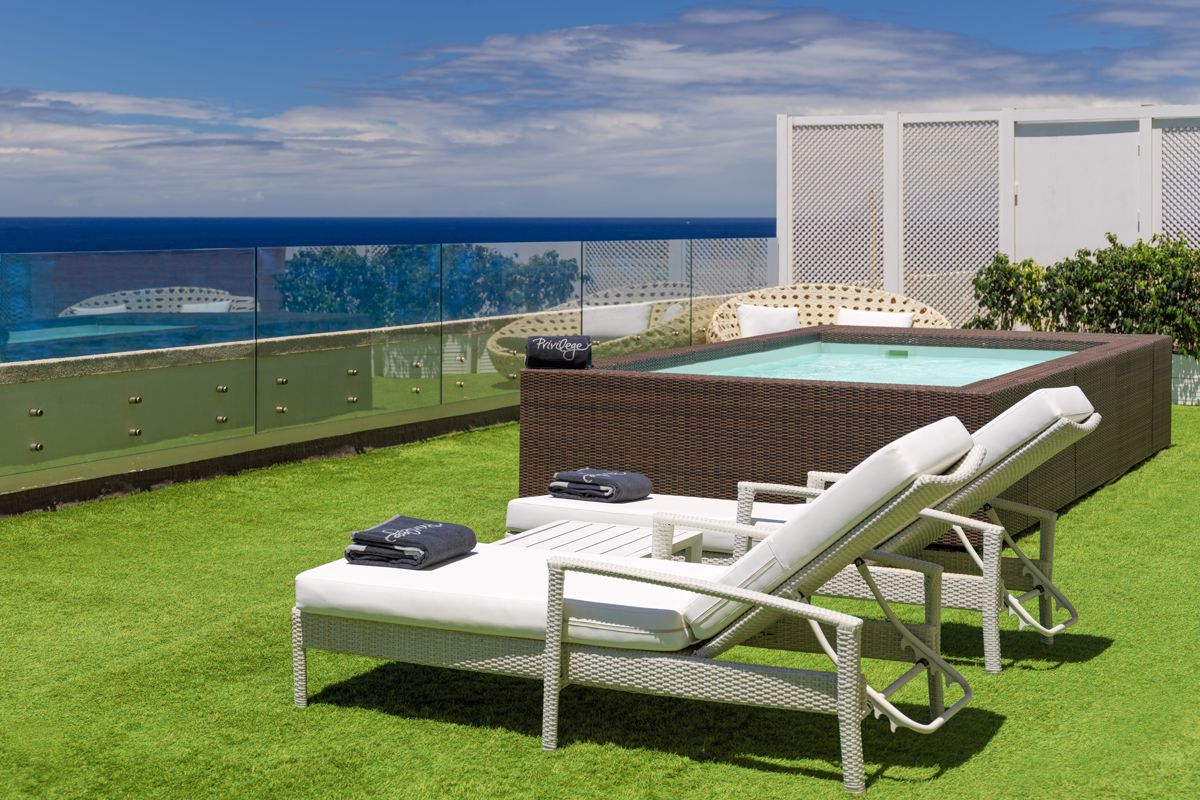 Loungers and a hot tub on a grass terrace with ocean view in Tenerife.