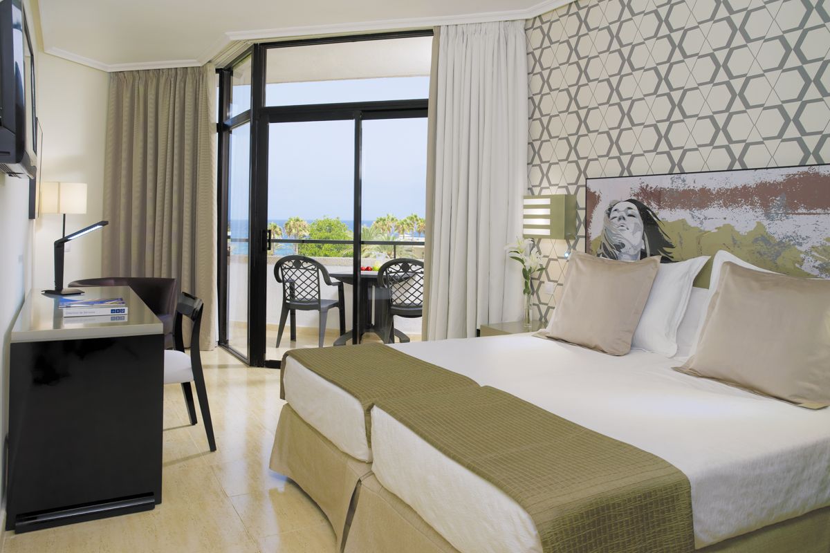 Hotel room with double bed, balcony view of palm trees and ocean in Tenerife.