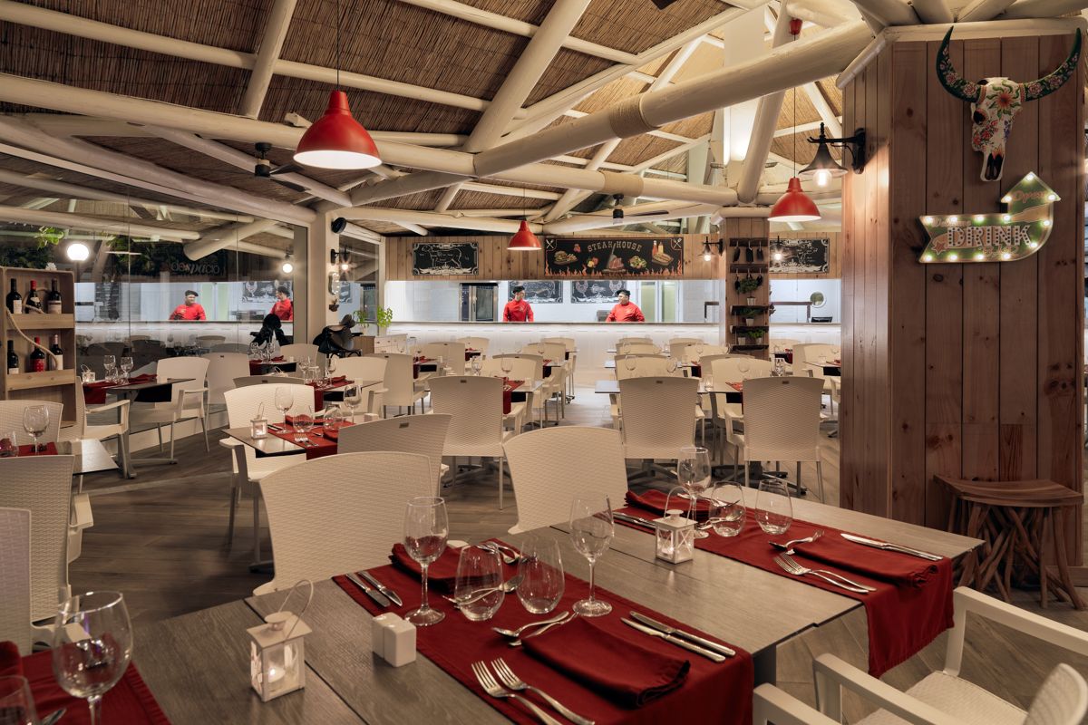 Restaurant interior with white tables, red napkins in Tenerife, chefs behind counter.