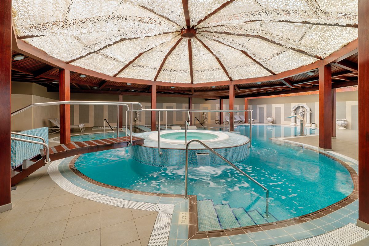 Indoor pool and jacuzzi at spa resort in Tenerife with wooden pillars and decorative ceiling.
