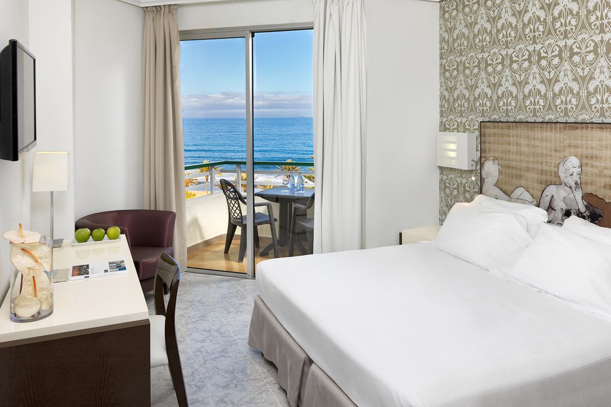Hotel room with ocean view and patio in Tenerife. Desk with lamp, apples, and decor.