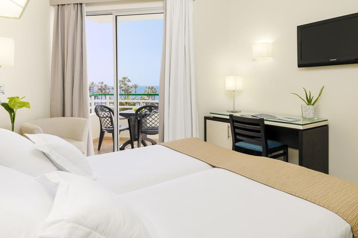 Hotel room in Tenerife with a bed, desk, and balcony overlooking the sea.