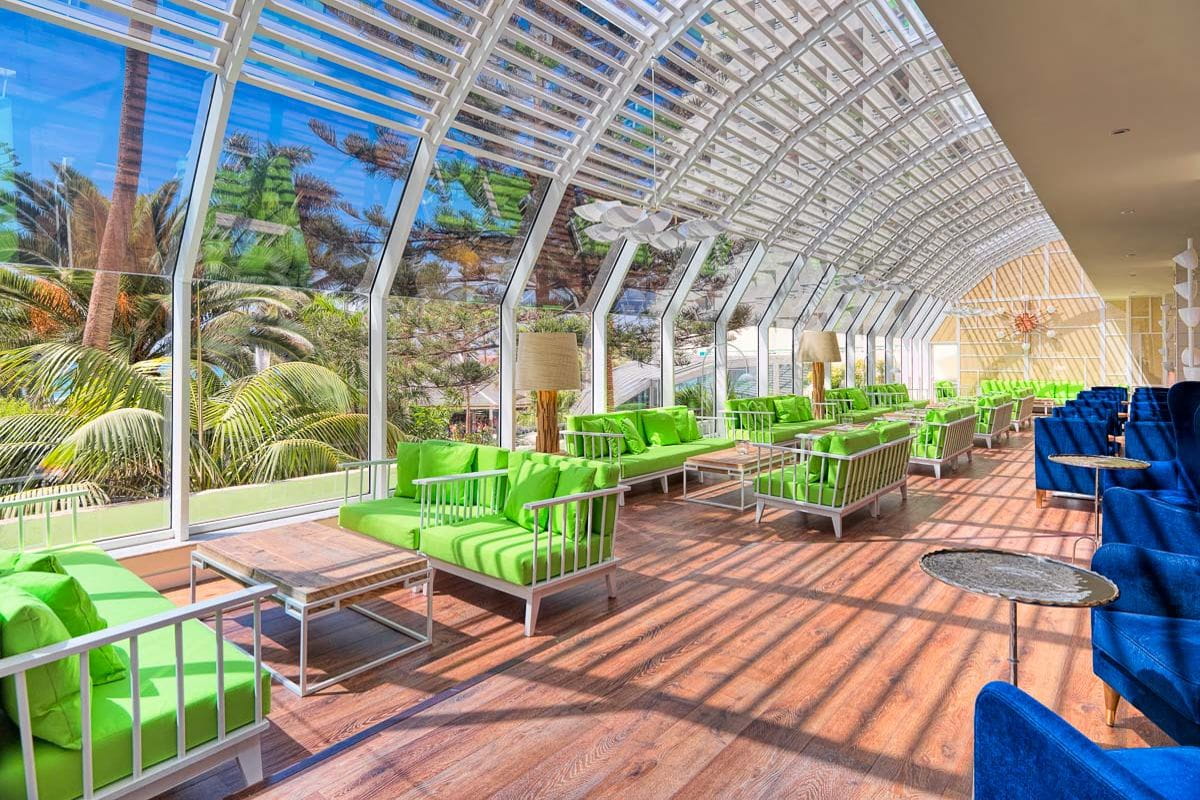 Spacious seating area with green sofas and glass ceiling in Tenerife building.