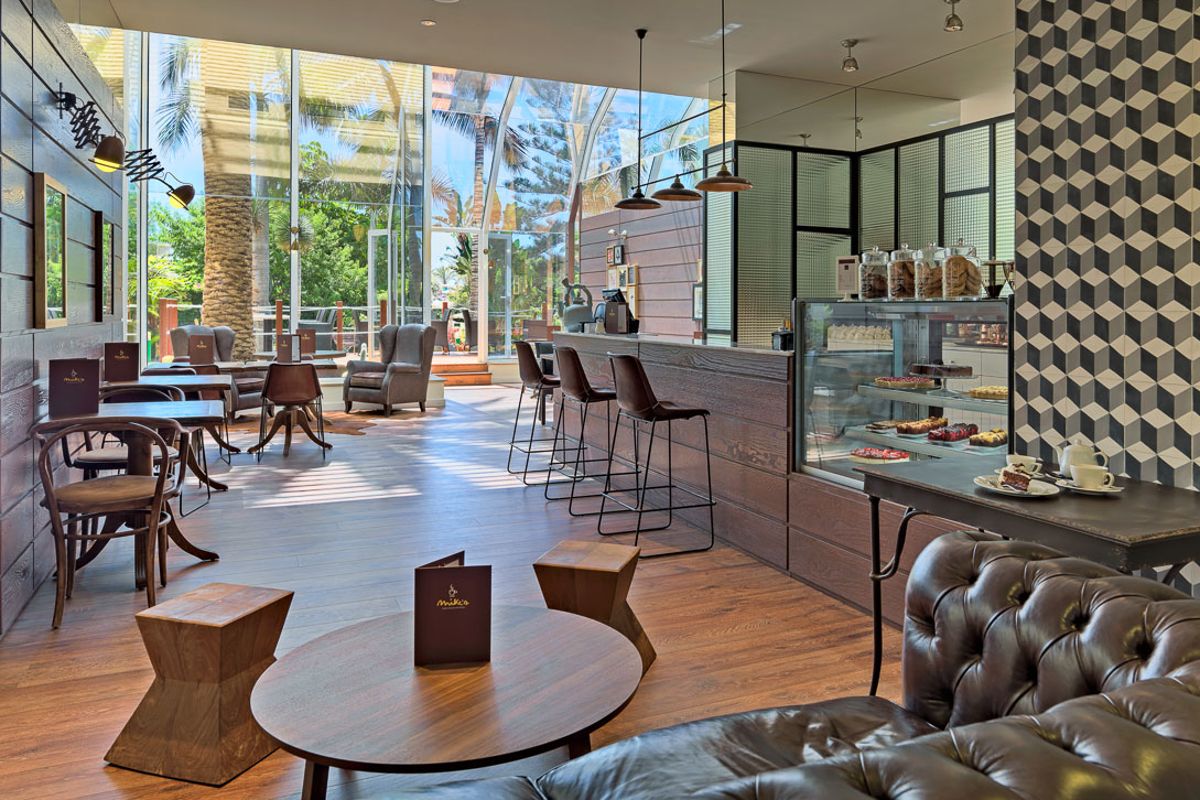 Modern café interior with wooden furniture, a dessert display, and outdoor views in Tenerife.
