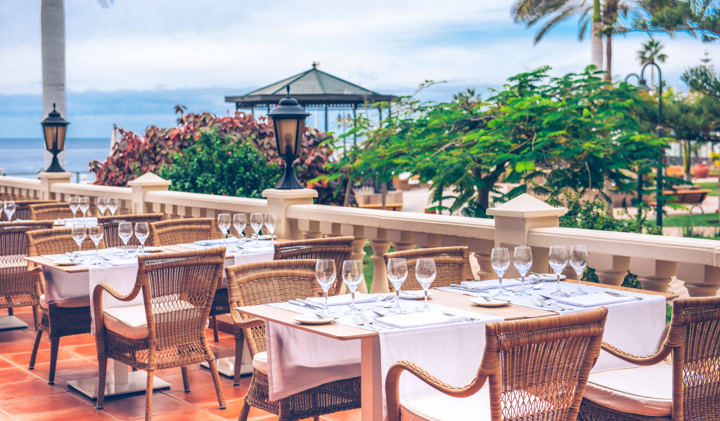 Outdoor dining setup with wicker chairs and tables overlooking the sea in Tenerife.