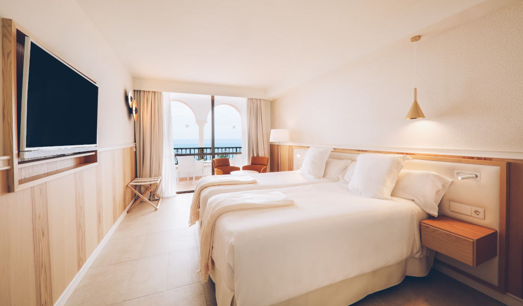 Two beds in a hotel room with balcony view in Tenerife.