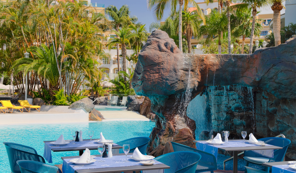Outdoor dining area by a waterfall pool at a Tenerife hotel.