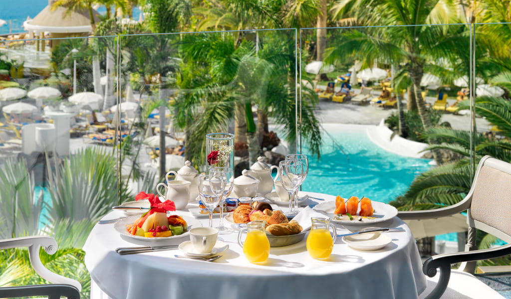 Breakfast table with fruits and juice overlooking pool in Tenerife.
