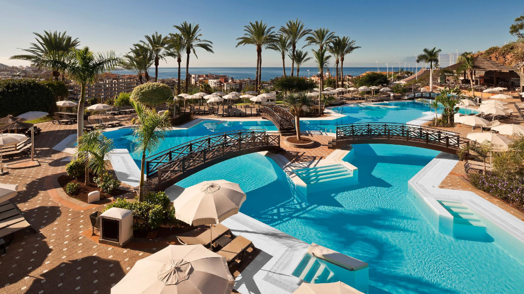 Outdoor swimming pool with bridges and palm trees in Tenerife resort.