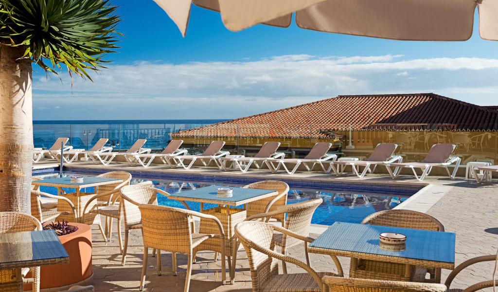 Outdoor terrace with tables, chairs, pool, and sea view in Tenerife.